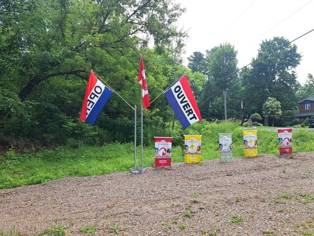 Drapeaux « Open » et « Ouvert » et sacs de moulée Campagnard à l'entrée de la ferme