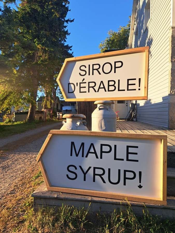 Panneaux « Sirop d'érable! » et « Maple syrup! » devant la maison, avec deux bidons de lait